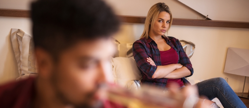 Angry Woman Sitting On Bed Behind Her Drunk Boyfriend