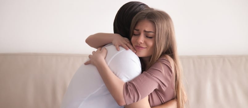 Retrato de jovem casal emocional se abraçando fortemente, namorado e namorada se abraçando sentados no sofá