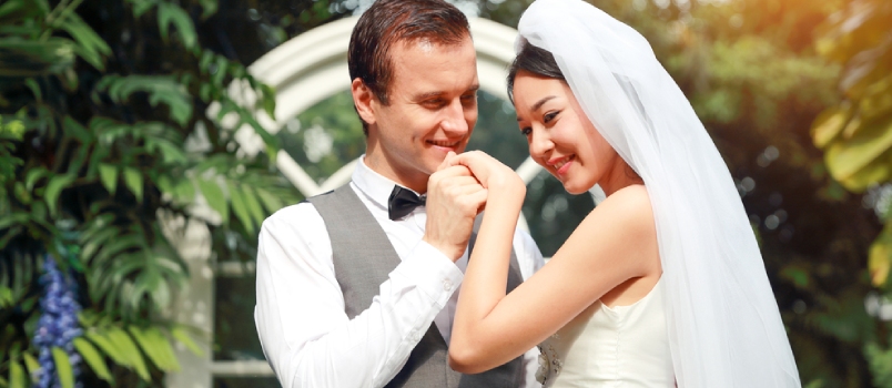Handsome Caucasian Groom Is Holding And Kissing Asian Bride Hand With Love And Smiling Face During Wedding