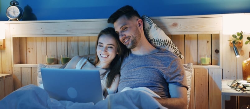 Attractive Affectionate Caucasian Couple At Home In Bed Streaming A Drama Film On Laptop Computer