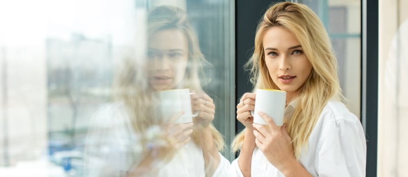 Beautiful Blonde Woman Standing Next To A Window, Wearing Men Shirt And Drinking Coffee