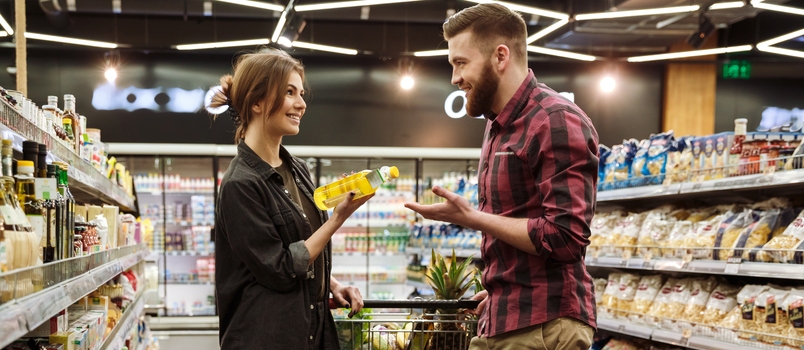 Picture Of Young Happy Loving Couple In Supermarket With Shopping Trolley Choosing Products. Looking Aside