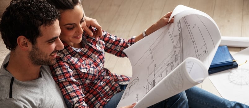 Young Couple Sitting On The Floor And Looking At The Blueprint Of New Home