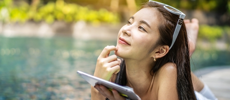 Beautiful Asian Woman With A Good Mood Playing A Tablet By The Pool And Think About The Past That Made It Happy