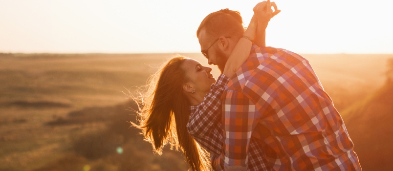 Man And Woman Tourists In The Mountains At Sunset. Happy Couple In Love.