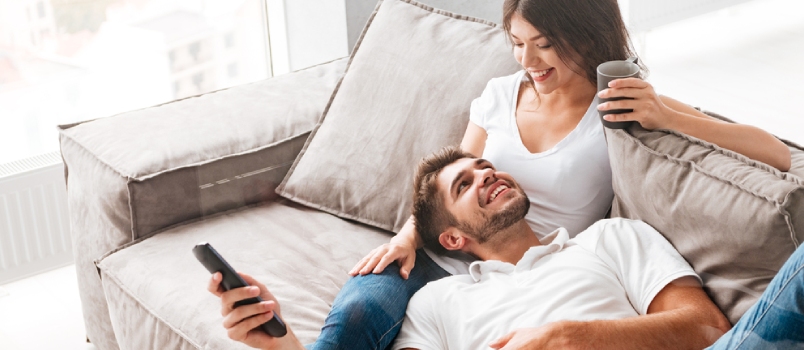Cheerful Beautiful Young Couple Drinking Coffee and Watching Tv at Home