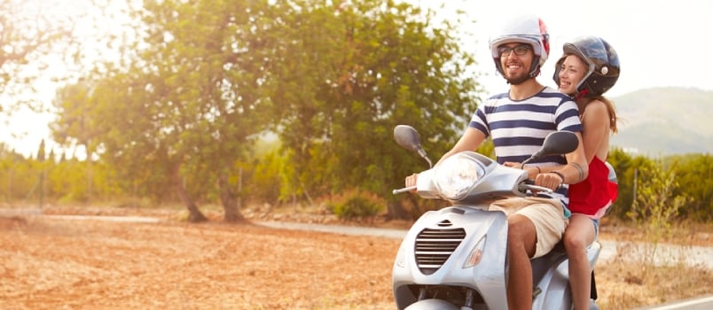 Young Couple Riding Motor Scooter Along Country Road