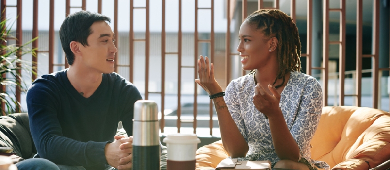Positive Emotional Young Businesswoman Discussing News and Ideas With Colleague at Meeting
