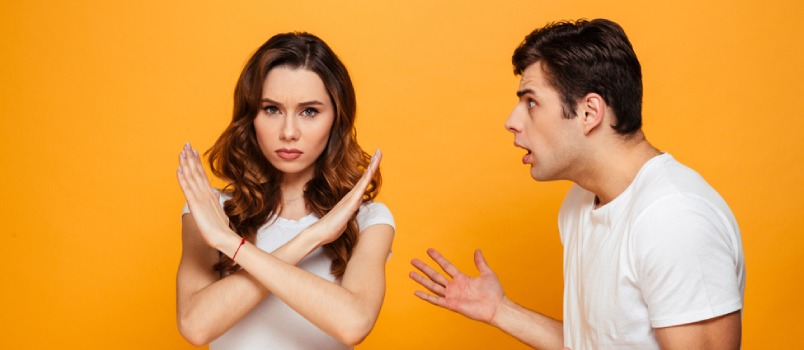 Displeased Man Screaming on His Girlfriend Which Showing Stop Gesture and Looking at the Camera Over Yellow Background