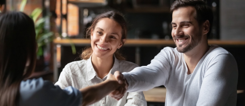 Happy Smiling Millennial Couple Handshake Get Acquainted With Female Real Estate Agent Meeting Together In Cafe