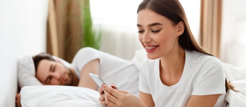 Cheating Wife Texting on Phone With Lover While Husband Sleeping Lying in Bed at Home