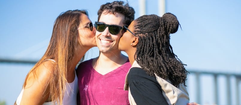 Joyful Old Friends Meeting and Having Fun Outside. Multiethnic Young Women Kissing Mans Cheeks