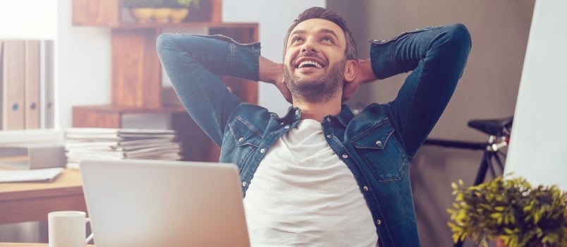 Happy Young Man Working on Laptop While Sitting at His Working Place in Office