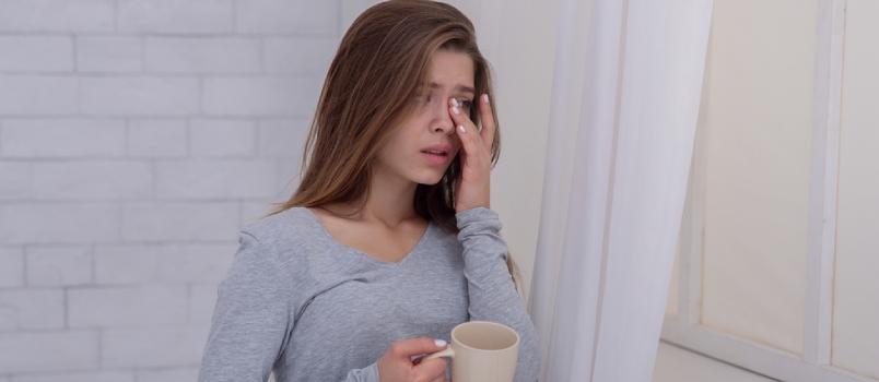 Unhappy Young Lady Standing Near Window With Cup of Coffee and Crying, Indoors