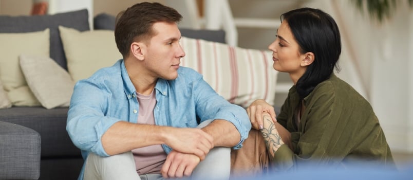 Warm Toned Portrait of Modern Young Couple Talking to Each Other Sincerely While Sitting on Floor in Cozy Home Interior, Copy Space