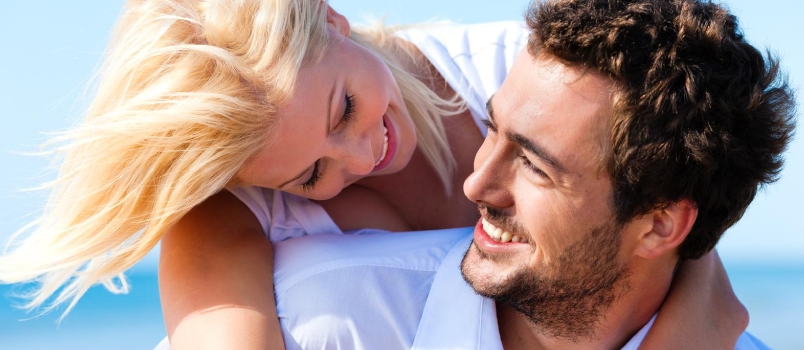 Couple in Love - Caucasian Man Having His Woman Piggyback on His Back Under a Blue Sky on a Beach
