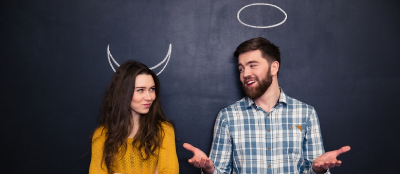 Smiling Young Man and Woman Imitating Devil and Angel Standing Over Chalkboard Background