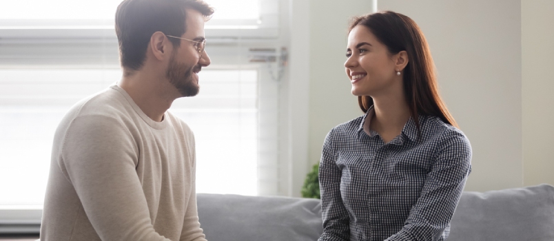 Happy Young Man Holding Attractive Woman Hands on Couch. Smiling Romantic Couple Enjoy Time Together.