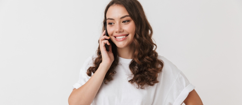 Portrait of a Smiling Young Casual Brunette Woman Talking on Mobile Phone Isolated Over White Background