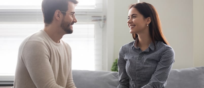 Happy Young Man Holding Attractive Woman Hands on Couch. Smiling Romantic Couple Enjoy Time Together