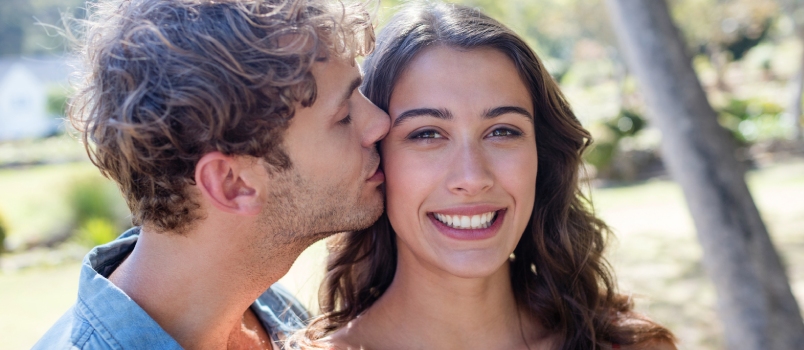 Man Kissing Woman on Cheek in Park on a Sunny Day
