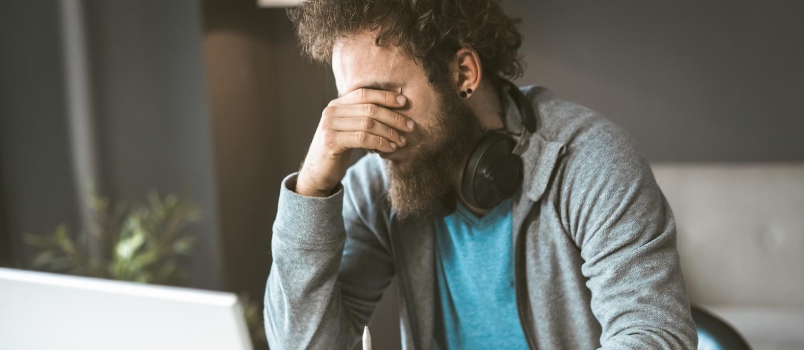 A Sad Man Sits in the Workplace Covering His Face With His Hand