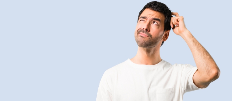 Young Man With White Shirt Having Doubts and With Confuse Face Expression While Scratching Head on Isolated Blue Background