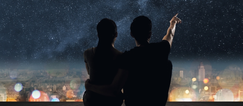 Silhouette of Couple Sit on Ground Point Faraway on the Roof Above the City in the Night.
