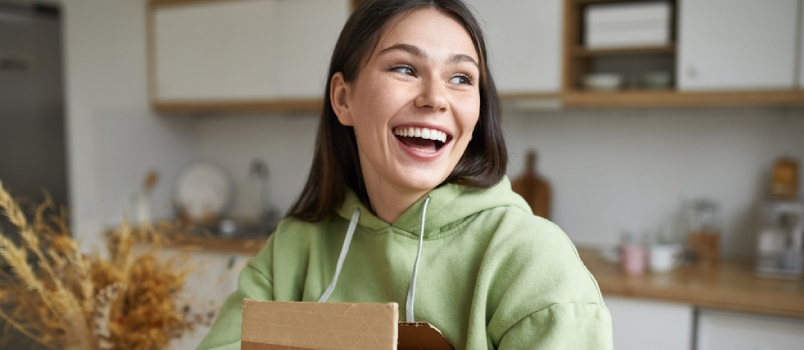 Happy Overjoyed Young Brunette Woman Posing Indoors With Small Cardboard Parcel in Her Hands With New Books