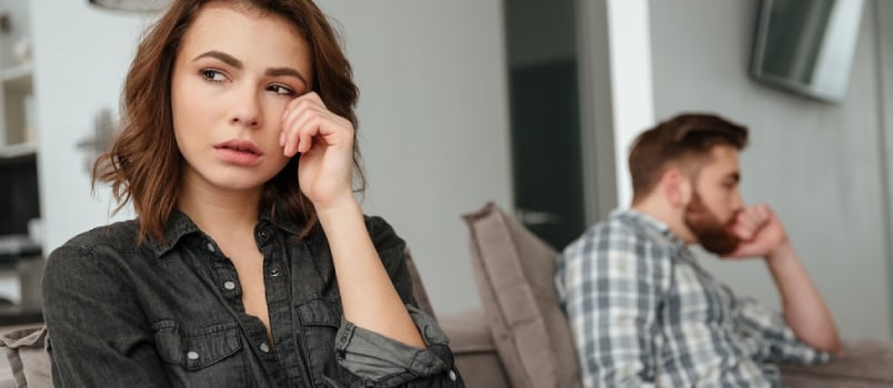 Focused Sad, Upset Lady Sitting Front at Home and Blurred Angry Man Sitting Behind on Some Distance