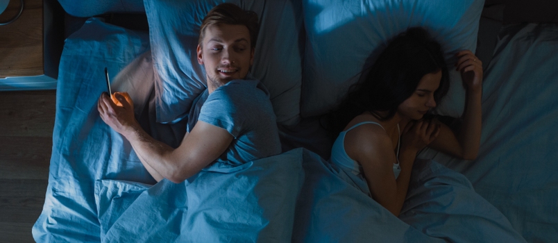 Cheating and Unfaithful Young Man Uses Smarphone for Finding a New Date or Bragging Night in Bed When Girlfriend Sleeps Soundly
