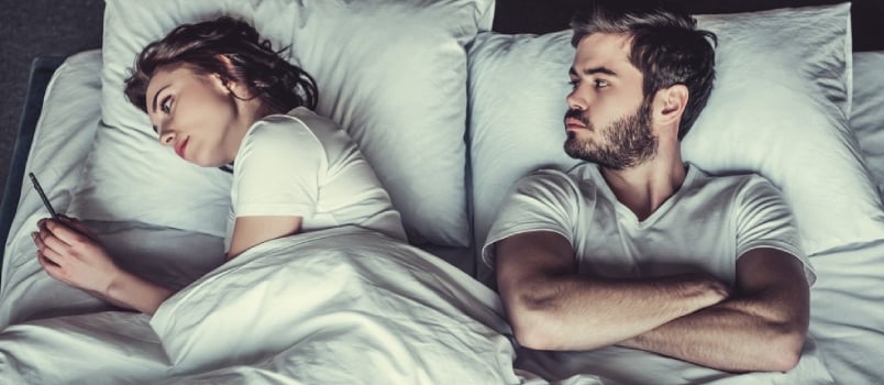 Young Unhappy Man and His Girlfriend Who Uses the Phone in Bed.