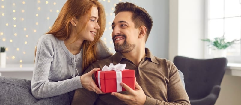 Side View of a Red-haired Young Woman With Her Husband Opening a Gift Box While Sitting at Home on the Couch