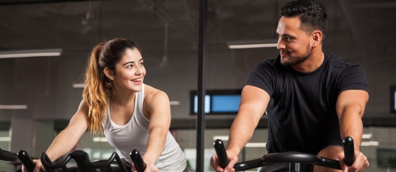 Beautiful Young Hispanic Woman Flirting and Talking to a Guy While They Both Do Some Spinning at a Gym