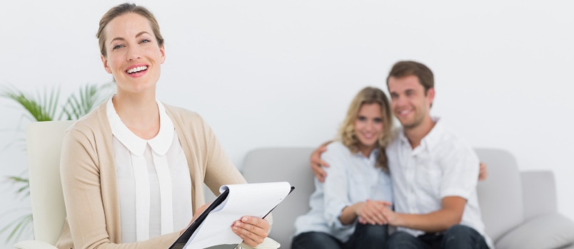 Financial Adviser Writing Notes With Young Couple in Background at Home