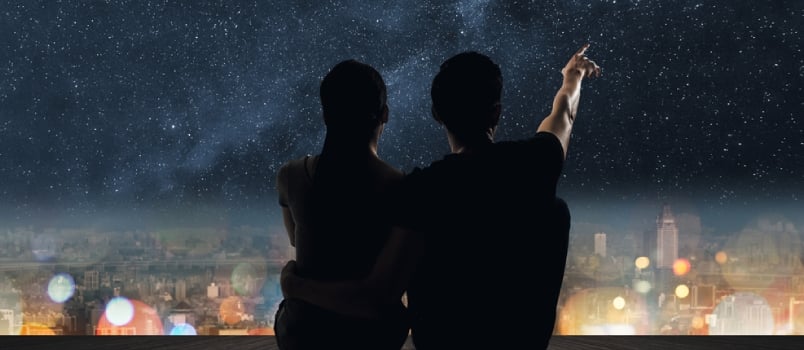 Silhouette of Couple Sit on Ground Point Faraway on the Roof Above the City in the Night.