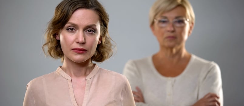 Sad Young Woman Looking in Camera, Strict Senior Mother Standing Behind