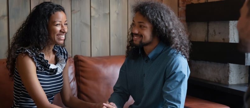 Couple Sitting on Couch at Counselor Office Looking in Each Other Eyes and Holding Hands Reconciling After Fight Giving Second Chance to Marriage
