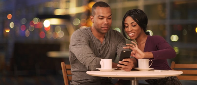 Happy Black Couple Using Smart Phone in Coffee Shop at Night