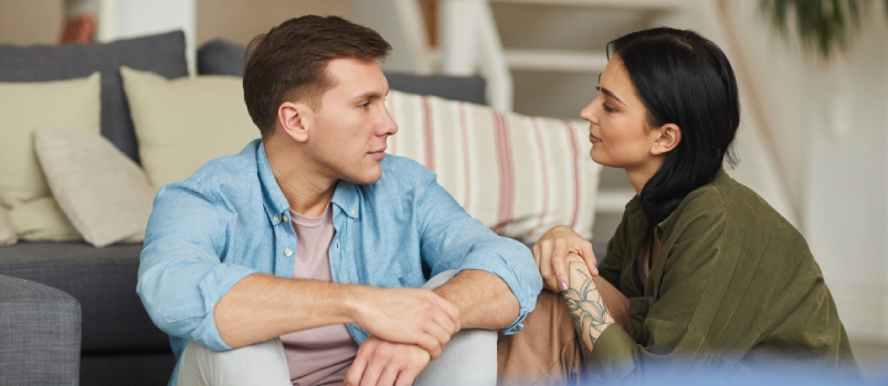 Warm Toned Portrait of Modern Young Couple Talking to Each Other Sincerely While Sitting on Floor in Cozy Home Interior