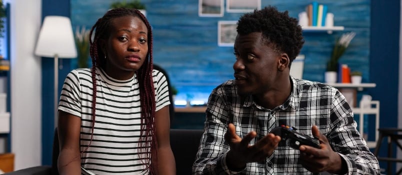 Disappointed black couple losing at video game on TV in living room