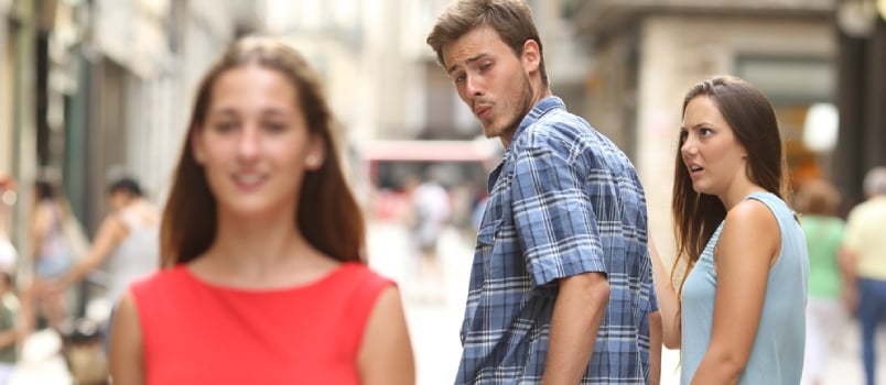 Disloyal man walking with his girlfriend and looking amazed at another seductive girl