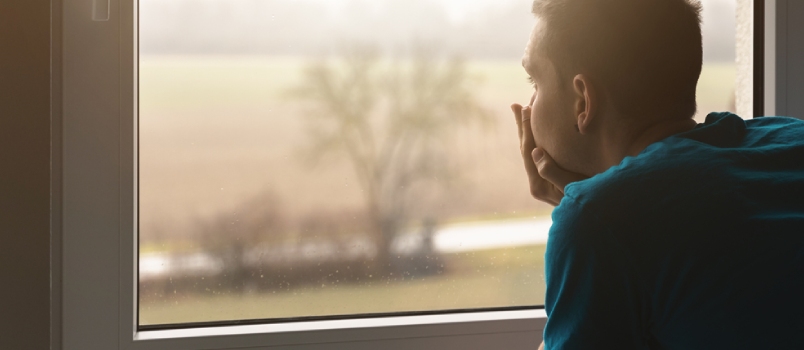 Sad Young Man at Home Looks Out of the Window. He Is Sad and Alone