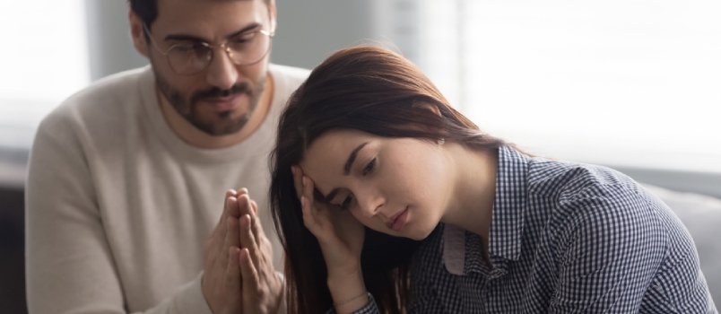 Head shot close up upset abused offended woman sitting on sofa, ignoring her apologizing husband. Young man feeling sorry, asking forgiveness to depressed wife