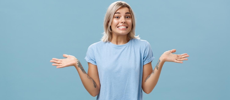 Oops I do not know. Silly cute european girl with fair hair and cool tattoos shrugging with palms spread