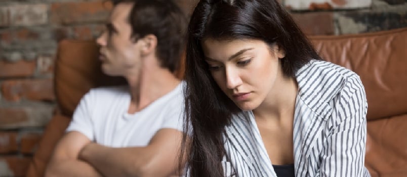 Sad pensive young girl thinking of relationships problems sitting on sofa with offended boyfriend