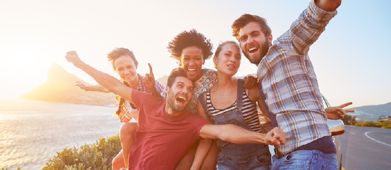Group Of Friends Standing By Car On Coastal Road At Sunset