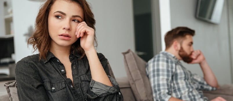 Photo of young sad quarrel loving couple sitting on sofa indoors. Looking aside
