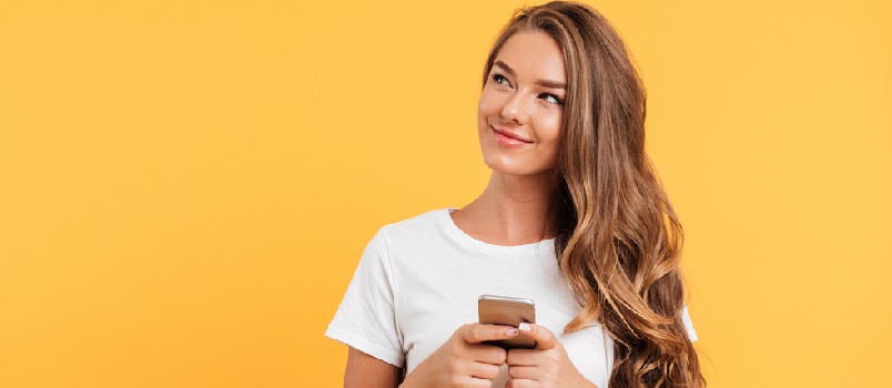 Photo of cheerful cute beautiful young woman chatting by mobile phone isolated over yellow wall background