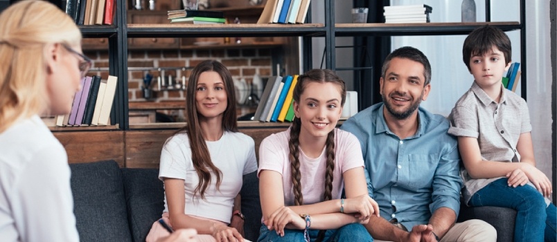 Smiling Family On Therapy Session By Female Counselor Writing In Clipboard In Office